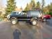 1995 Ford Bronco - A black 1995 Ford Bronco is parked on a wet asphalt surface, with a red pickup truck behind it.