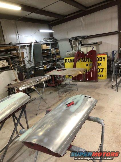 Car doors and body panels being worked on in a workshop with a sign for Ramsey Auto Body