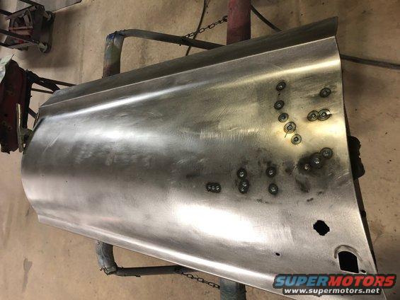 Bare metal car door panel with numerous spot welds and cutouts for hardware