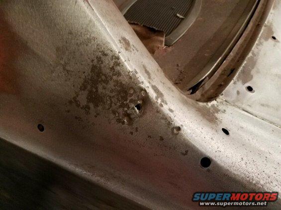 Metal car part with rust spots and drilled holes, showing a section of a grille
