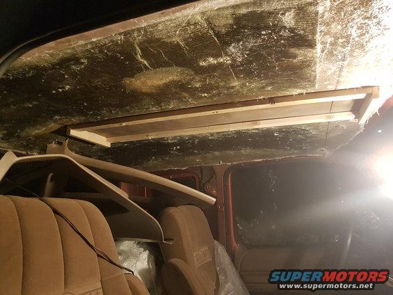 Interior of a vehicle with brown seats and a wooden shelf installed on the ceiling