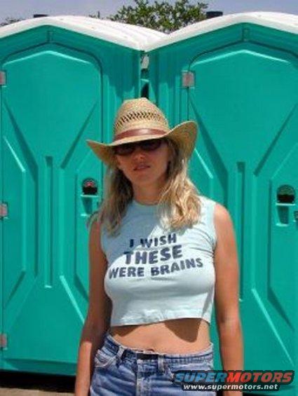 woman wearing a cowboy hat and a crop top that says 'I wish these were brains', standing in front of two portable toilets