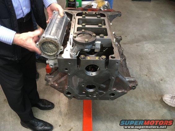 Engine block on an orange stand with a person holding an oil filter housing