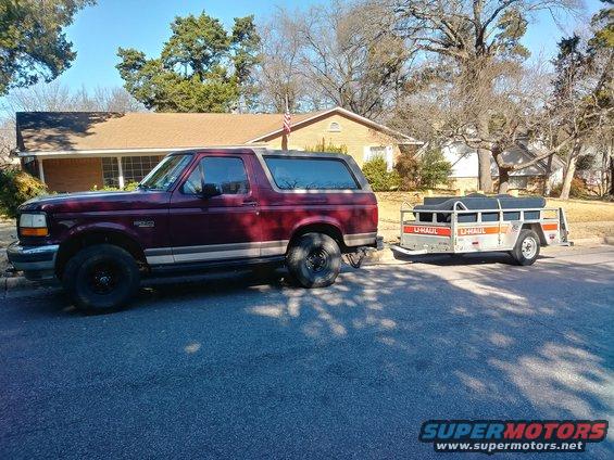 Maroon Ford Bronco parked on street, towing a U-Haul trailer