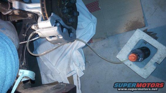 Brake caliper with bleeder hose connected to a bottle on a concrete block