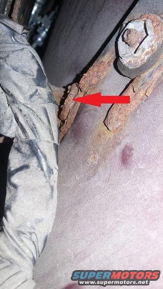 Close-up of a rusted metal bracket with a red arrow pointing to it, next to a black wiring harness