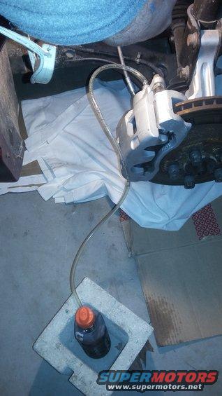 Brake caliper with bleed tube draining fluid into bottle on concrete floor