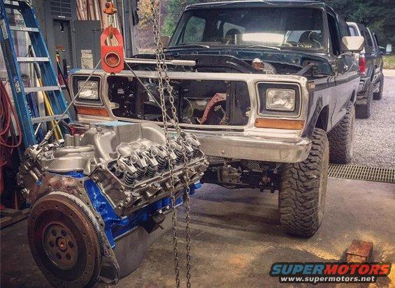 Ford Bronco in garage with engine being lifted out. Another truck is behind it