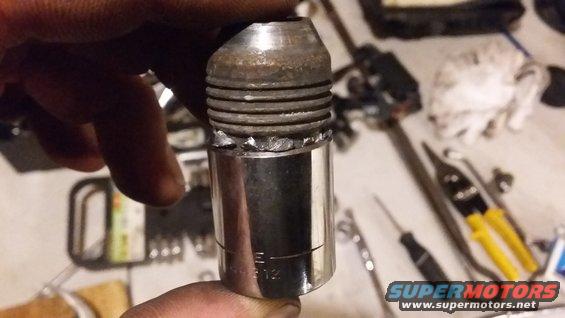 Spark plug socket welded to a threaded extension, held by a hand. Tools are visible in the background