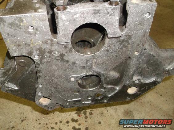 Gray engine block with oil stains on concrete floor. Visible bolt holes and circular openings