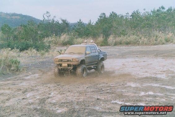 Lifted pickup truck driving through mud, looks like an older Toyota Hilux
