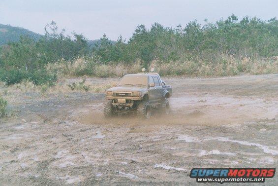 Mud-covered Toyota pickup truck with large tires driving through a muddy field