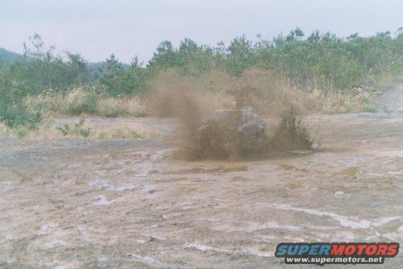 Truck driving through a muddy area, kicking up a lot of spray