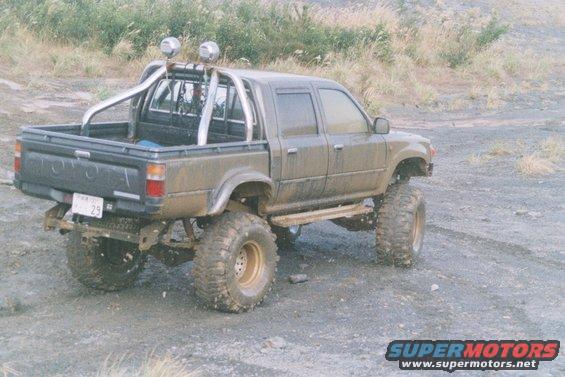 Lifted Toyota pickup truck with roll bar and large tires, parked on dirt