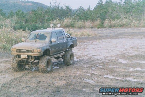 Dark gray Toyota pickup truck with lifted suspension and large tires, parked in mud