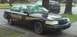 1998 Ford Crown Victoria - A black 1998 Ford Crown Victoria police car with a gold stripe is parked on a driveway, showing some damage to the front fender.
