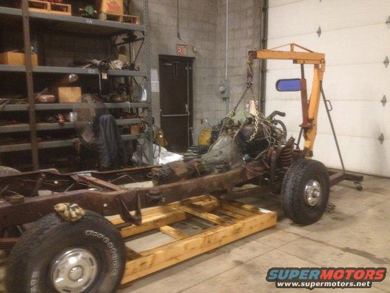 1979 Ford Bronco frame on wooden supports, engine suspended by an engine hoist