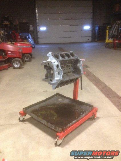 Engine block on a red rolling stand with a drip pan underneath, in a garage