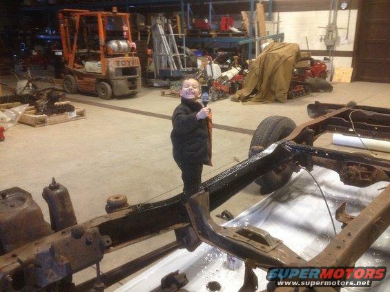 kid holding paintbrush in front of rusty vehicle frame