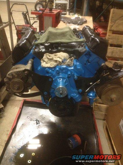 Blue and black engine assembly on a red oil drain pan, with an alternator and pulleys visible