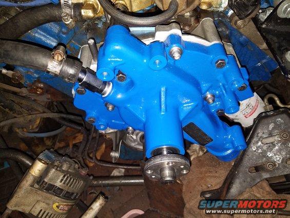 Blue painted engine water pump with black hose attached, showing alternator and engine block