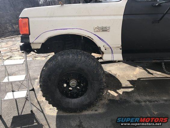 White and black Ford F-250 fender with purple markings, large off-road tire, and ladder