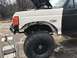 1989 Ford Bronco - A white Ford F-250 with a damaged front fender and a large off-road tire is shown, with the hood open and tools nearby.