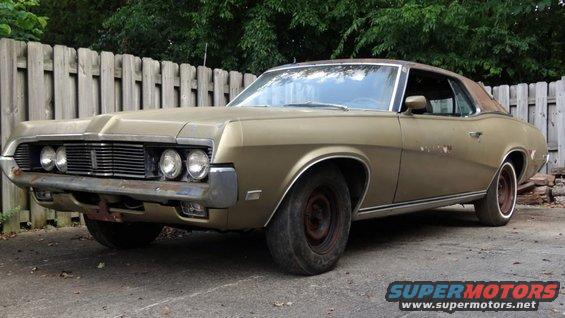 Gold 1969 Mercury Cougar coupe with a rusty front bumper and aftermarket wheels parked outdoors