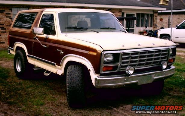 1980 Ford Bronco parked on grass in front of a brick house, brown and cream two-tone paint