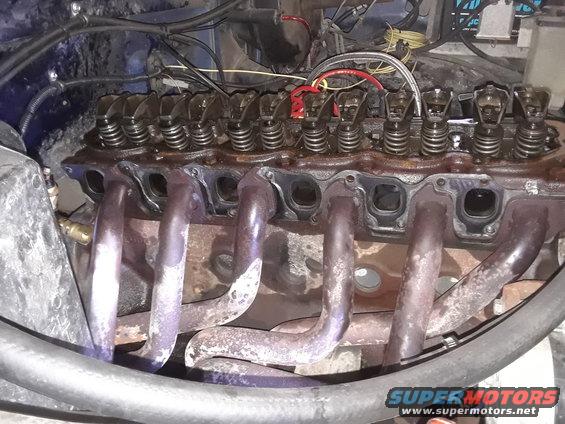 Close-up of engine cylinder head with exhaust manifold attached. Shows valves and springs