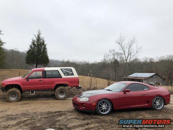 Lifted red 1984 Toyota 4Runner and a red Toyota Supra parked on a dirt road