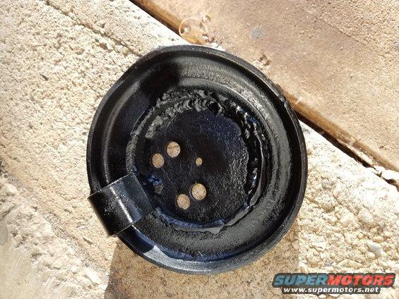 Black metal brake drum with visible welds and mounting holes, resting on concrete