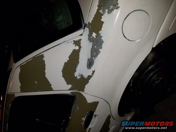 Side view of a white car with peeling paint showing primer and olive drab underneath