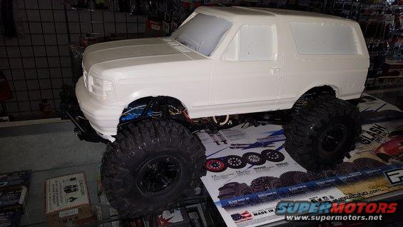 White RC car body, unpainted, with large off-road tires, viewed from the front-right