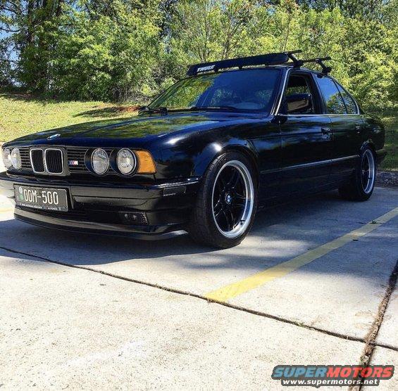 Black BMW sedan with a Thule roof rack, custom wheels, and a license plate reading OOM-500