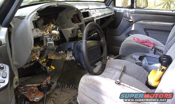 1995 Ford Bronco interior with dashboard removed, showing wiring and components. Steering wheel and seats are visible