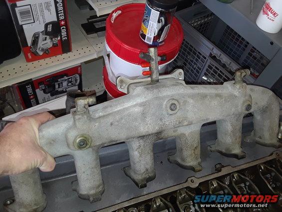 Aluminum intake manifold with four runners, held by a hand over engine components