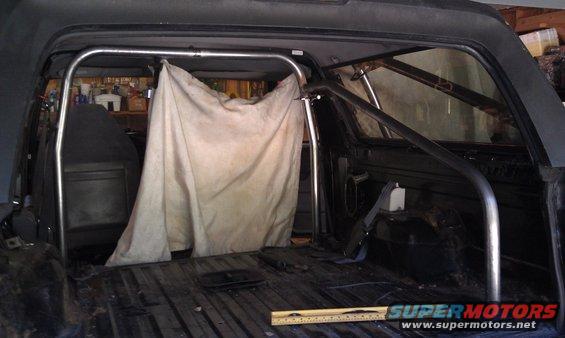 1995 Ford Bronco interior with roll cage installed and a tarp covering part of the cage