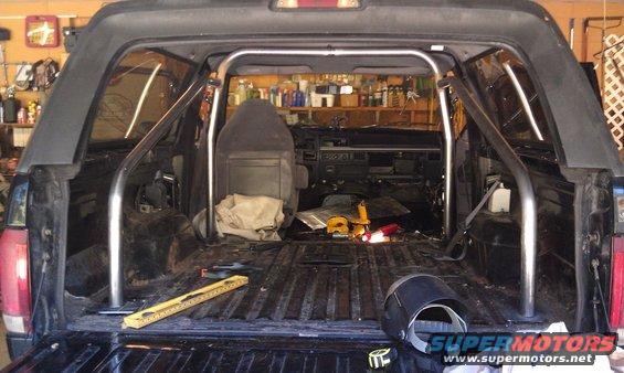 Interior of a black Ford Bronco with a roll cage installed, showing the dashboard and empty cargo area. Tools are visible