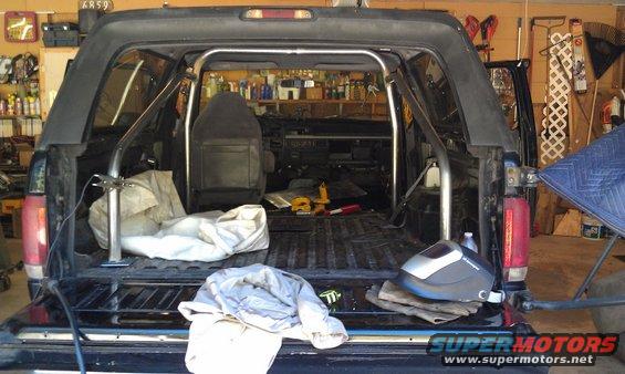 Black Ford Bronco interior with a custom roll cage, seats, and welding helmet. The tailgate is open