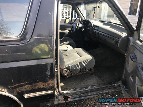Dark gray 1992 Ford Bronco interior with ripped driver's seat and rust on the door sill