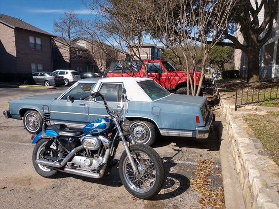 Blue sedan parked next to a red pickup truck. Motorcycle in foreground