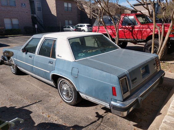 Blue sedan with a white roof, seen from the rear, with a red truck behind it