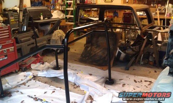 Black roll cage installed inside a garage, with car parts and tools in the background