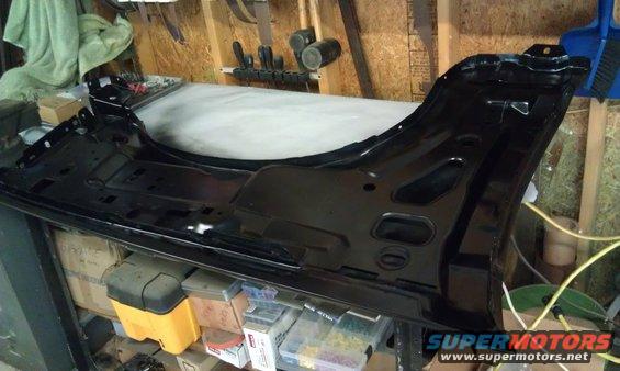 Black metal fender assembly with mounting brackets and cutouts, resting on a workbench