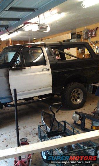 Side view of a black and white 1995 Ford Bronco with its driver's door open, parked in a garage