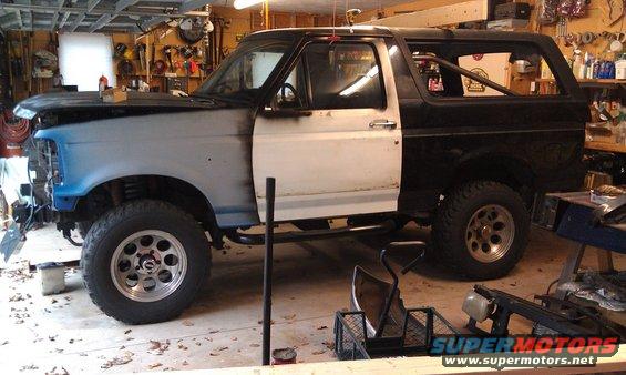 1995 Ford Bronco in a garage, with primer on the front fenders and hood, and the driver's door open