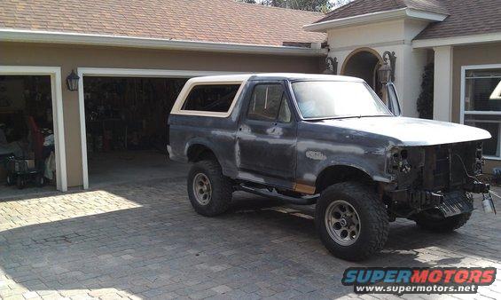 1980 Ford Bronco with a white topper parked in front of a garage