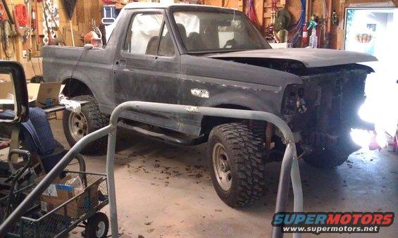 Gray Ford Bronco in garage, hood open, front end disassembled, off-road tires