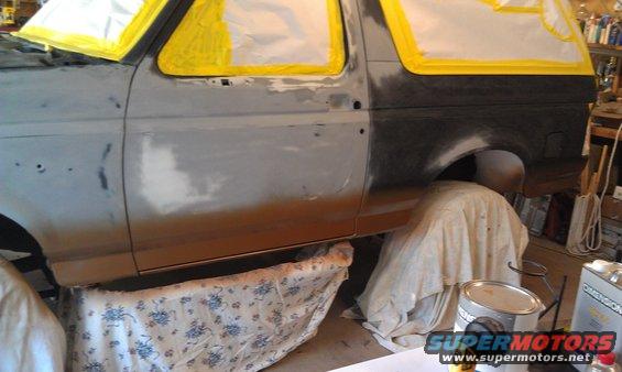 Gray Ford Bronco undergoing bodywork, with yellow masking tape around windows and doors